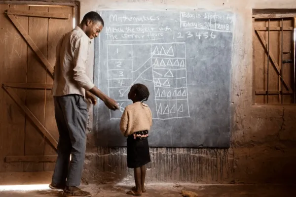 Docent geeft een krijtje aan een leerlinge.