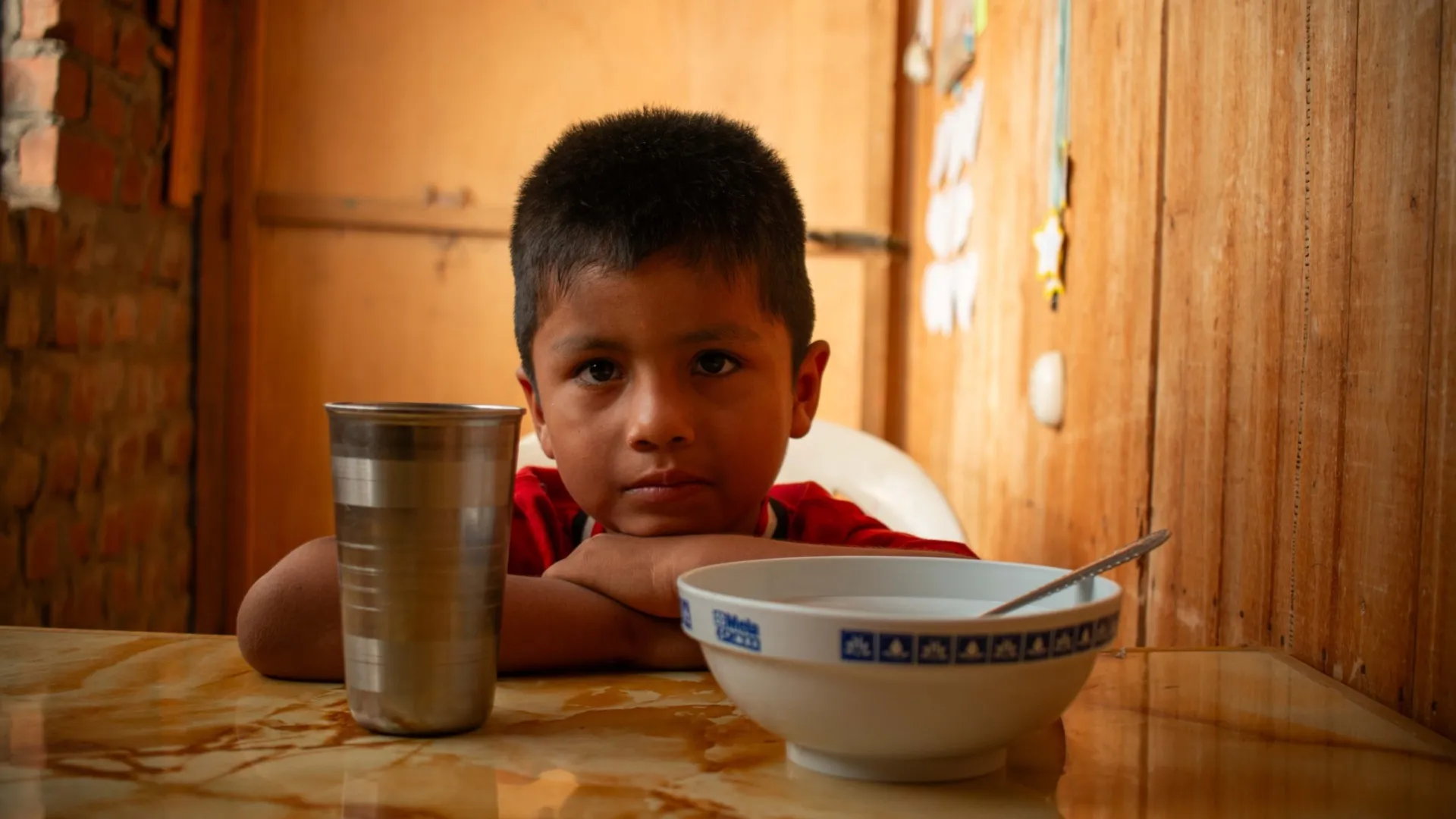 Een Peruaans jongetje zit achter een eettafel.